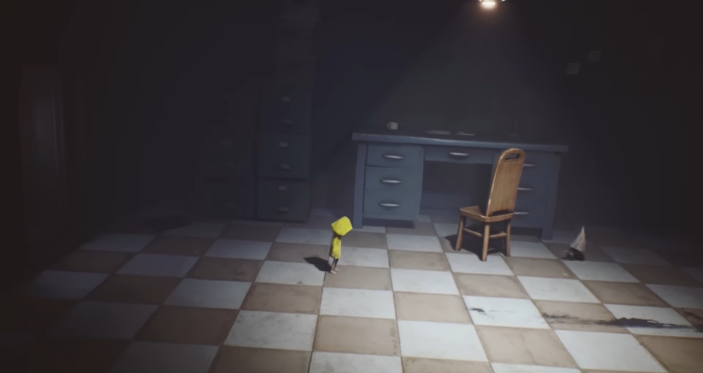 Шестая из Little Nightmares стоит в комнате с столом