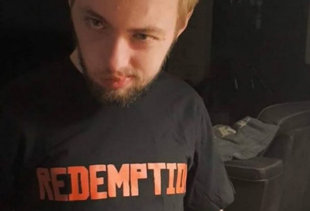 Мужчина в чёрной футболке Redemptio сидит в комнате