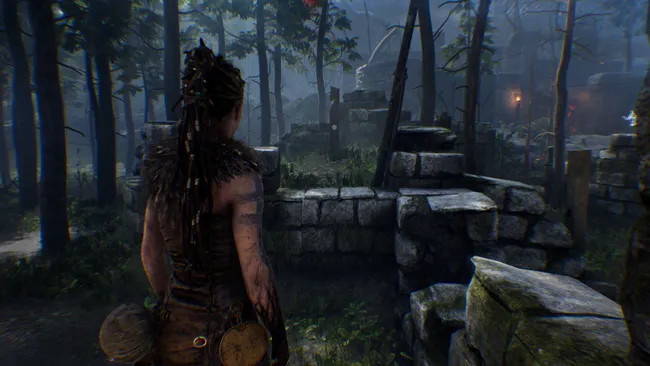 Сенуа из Hellblade стоит у каменной стены в лесу