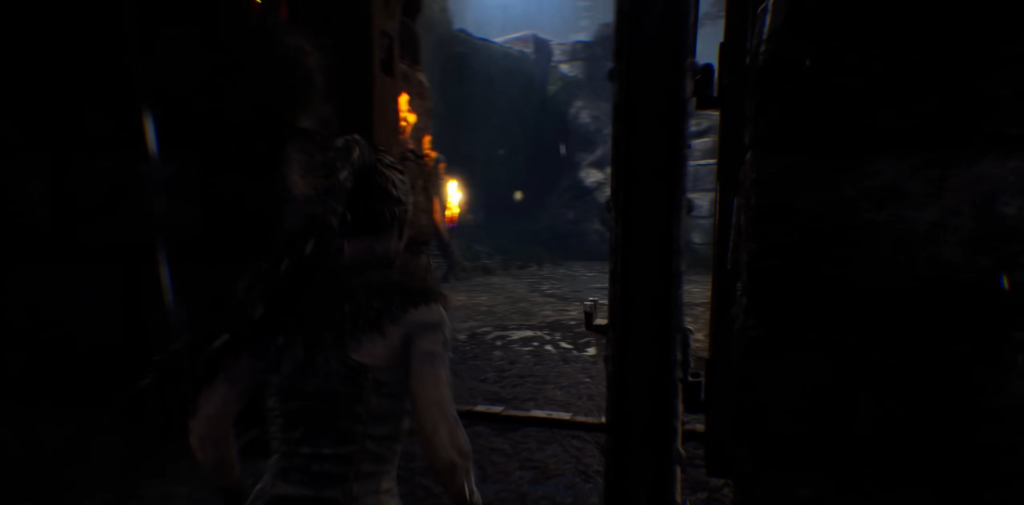 Сенуа из Hellblade идет по темной пещере с факелами